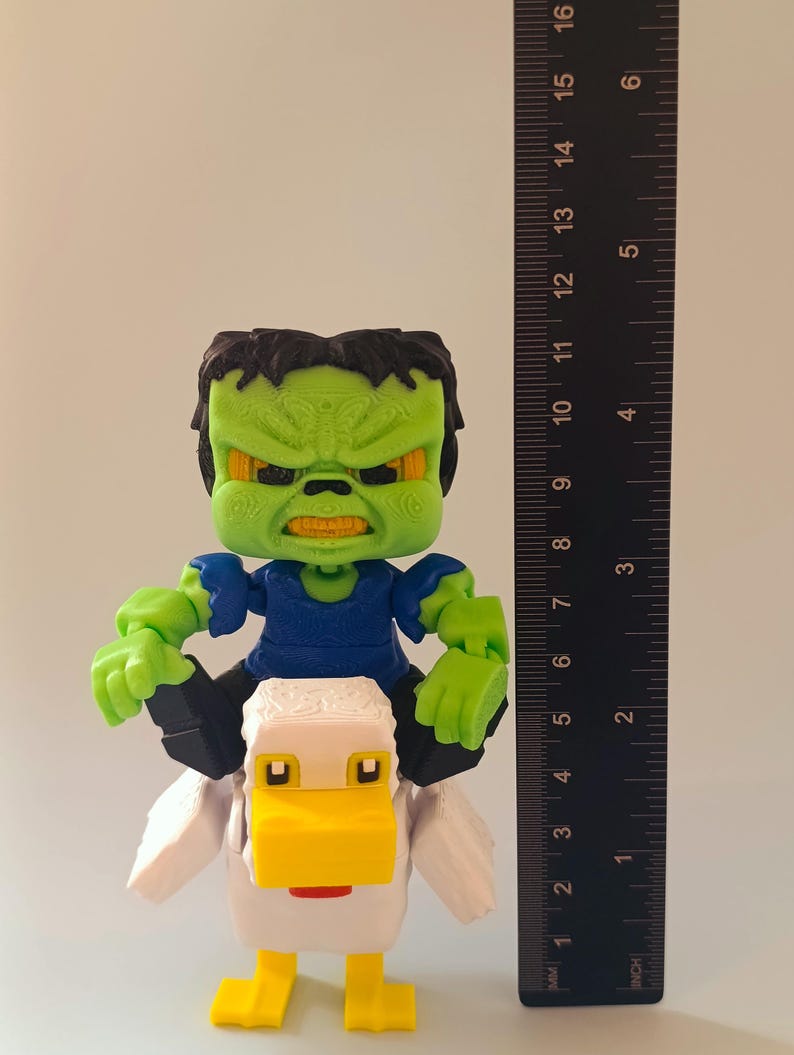 May include: A 3D-printed figurine of a green-skinned character with black hair and a blue shirt riding a white and yellow duck. The figurine is approximately 4 inches tall, with a ruler in the background for scale.