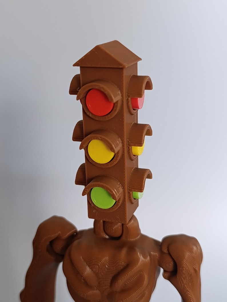 May include: A brown 3D-printed sculpture of a traffic light with a humanoid body. The traffic light head has red, yellow, and green lights. The figure has arms and a textured surface.