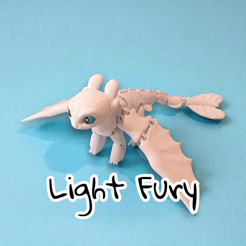 May include: A light-colored, articulated dragon figurine with large wings and a long tail, set against a blue background. The text "Light Fury" is written in a black, handwritten font at the bottom of the image.