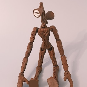 Op de afbeelding: Een bruine Siren Head actiefiguur met een uniek hoofdontwerp met een luidsprekerachtige mond en twee oorachtige structuren. De figuur heeft beweegbare ledematen en een gedetailleerd, getextureerd lichaam.
