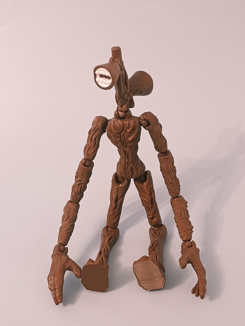 Op de afbeelding: Een bruine Siren Head actiefiguur met een uniek hoofdontwerp met een luidsprekerachtige mond en twee oorachtige structuren. De figuur heeft beweegbare ledematen en een gedetailleerd, getextureerd lichaam.