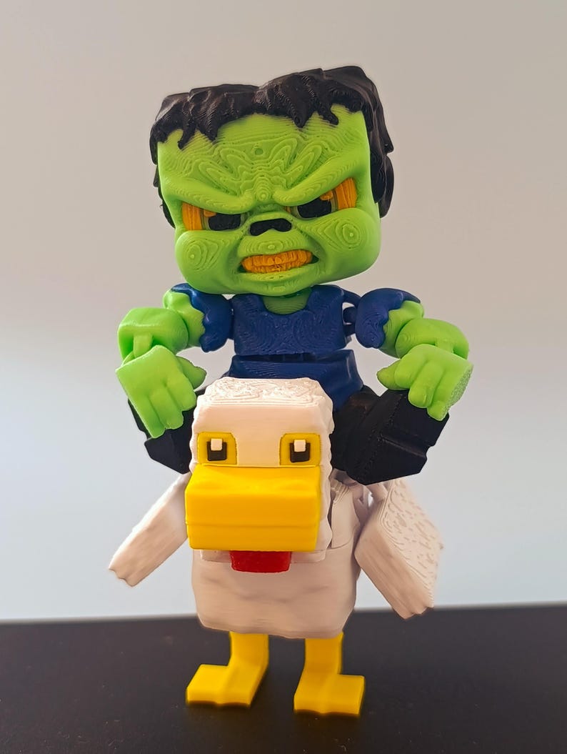 May include: A 3D-printed toy featuring a green-skinned monster riding a white and yellow pixelated chicken. The monster has black hair, a blue shirt, and an angry expression. The chicken has a red wattle.