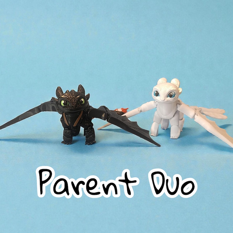 May include: Two dragon figurines, one black and one white, with outstretched wings, stand on a blue background. The black dragon has green eyes and the white dragon has blue eyes. The text "Parent Duo" is at the bottom.