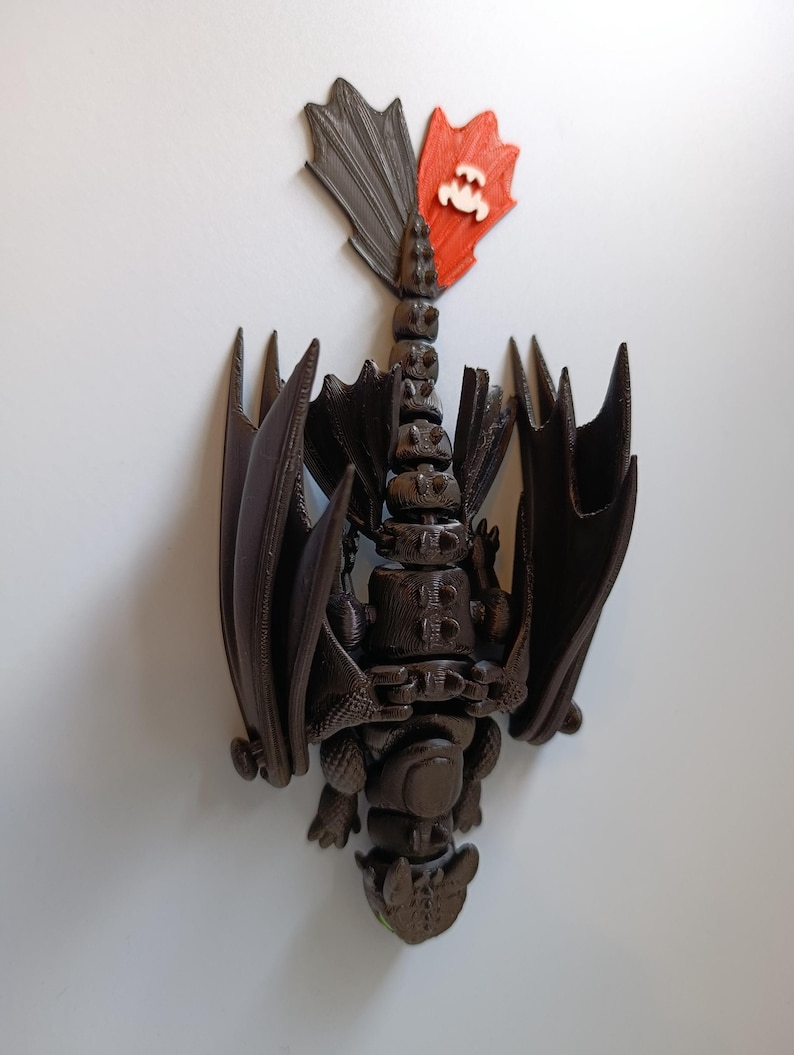 K&ouml;nnte beinhalten: Braune Drachenfigur mit ausgebreiteten Fl&uuml;geln und einem segmentierten K&ouml;rper. Der Drachenschwanz hat eine rote und graue Flosse mit einem wei&szlig;en Emblem. Die Figur ist eine detaillierte, dreidimensionale Darstellung eines Drachen.