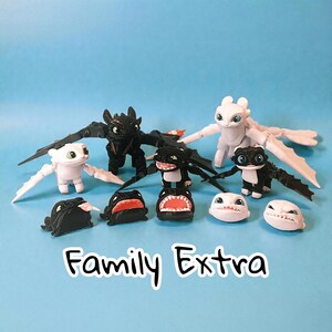 May include: A collection of dragon figurines in black and white, with articulated wings and various facial expressions. The text "Family Extra" is displayed in a playful font on a blue background.