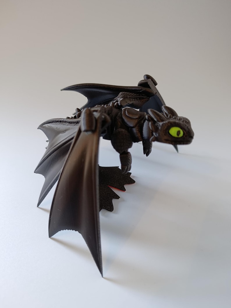 K&ouml;nnte beinhalten: Eine schwarze Drachenfigur mit weit ausgebreiteten Fl&uuml;geln und detailliertem K&ouml;rper. Der Drache hat leuchtend gr&uuml;ne Augen und scheint zu fliegen. Die Figur steht vor einem schlichten wei&szlig;en Hintergrund.
