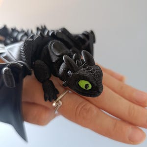 K&ouml;nnte beinhalten: Schwarze Drachenfigur mit gr&uuml;nen Augen und detaillierten Fl&uuml;geln. Der Drache sitzt auf einer Oberfl&auml;che und zeigt sein strukturiertes Design. Die Figur ist ein Sammlerst&uuml;ck zum Thema Fantasy.
