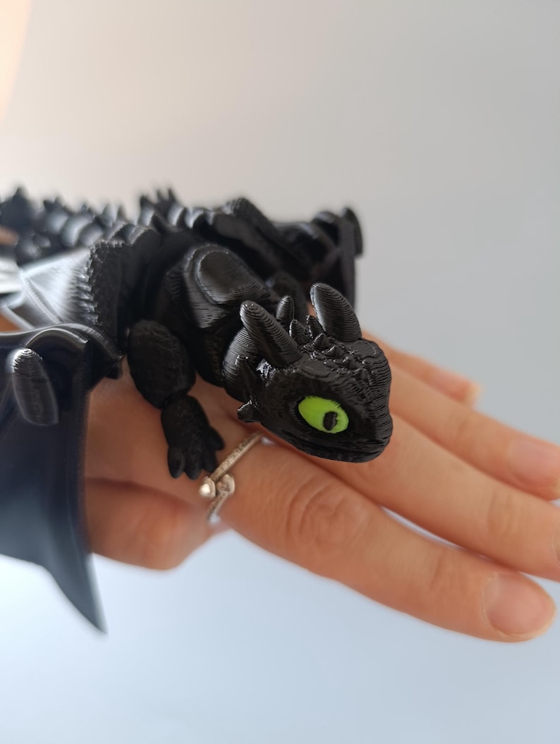 K&ouml;nnte beinhalten: Schwarze Drachenfigur mit gr&uuml;nen Augen und detaillierten Fl&uuml;geln. Der Drache sitzt auf einer Oberfl&auml;che und zeigt sein strukturiertes Design. Die Figur ist ein Sammlerst&uuml;ck zum Thema Fantasy.