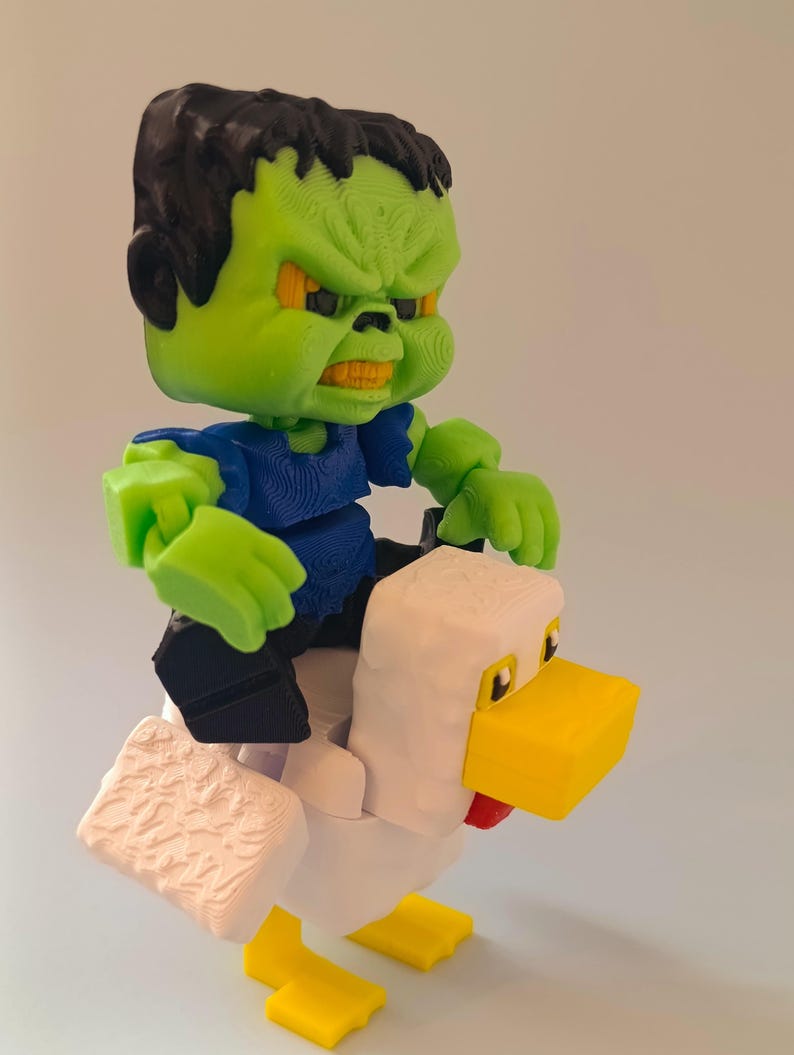 May include: A 3D-printed toy featuring a green monster figure with black hair and an angry expression, riding a white chicken with yellow beak and feet. The monster wears a blue shirt and black pants.
