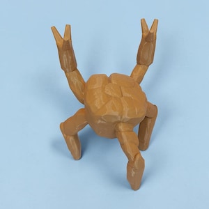 Pode incluir: Estatueta de caranguejo castanho com garras e pernas levantadas, sobre um fundo azul claro. O corpo do caranguejo tem um design texturizado e segmentado. A estatueta &eacute; um item decorativo.