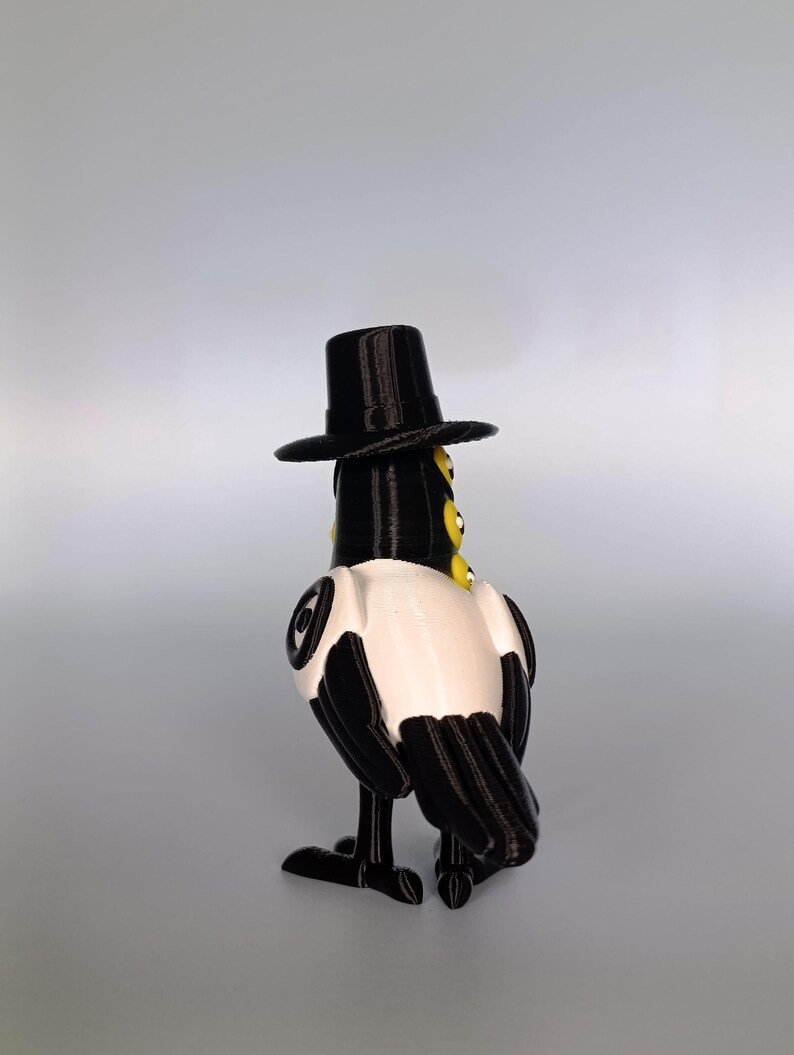Puede incluir: Figura impresa en 3D de un p&aacute;jaro con sombrero de copa negro. El p&aacute;jaro tiene un cuerpo negro con detalles blancos en el pecho y las alas. Tiene ojos amarillos y se ve desde atr&aacute;s.