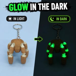 May include: A brown and white articulated spider keychain with a metal ring. The text GLOW IN THE DARK appears at the top, with IN LIGHT and IN DARK labels. The spider appears brown in light and emits a bright green glow in the dark.
