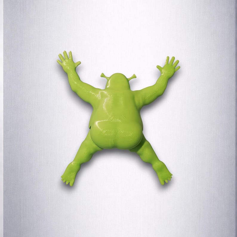 Puede incluir: Una figura verde de Shrek en pose de escalada, con los brazos y las piernas extendidos. La figura es de color verde vibrante y tiene un acabado liso y brillante. El fondo es de color gris claro.