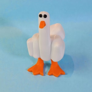 May include: A white goose figurine with orange feet and beak, set against a light blue background. The goose has black eyes and a long neck. The wings are slightly spread, giving the impression of movement. A whimsical decorative item.
