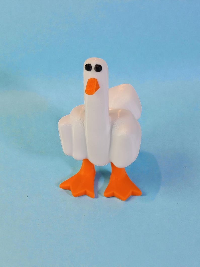May include: A white goose figurine with orange feet and beak, set against a light blue background. The goose has black eyes and a long neck. The wings are slightly spread, giving the impression of movement. A whimsical decorative item.