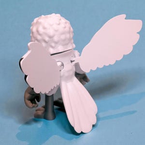 May include: A white figurine of a bird with large, stylized wings and a textured head. The bird has gray legs and a tail, set against a light blue background. The wings are spread, and the figure is viewed from the back.