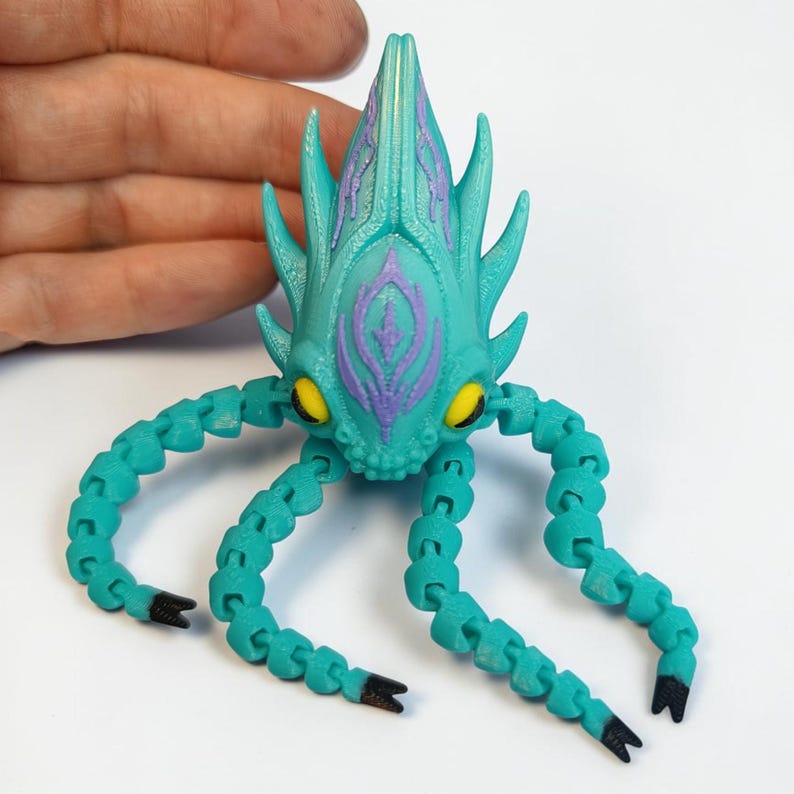 May include: A teal articulated creature toy with a spiky head and segmented tentacles. The head features purple accents and yellow eyes. The tentacles have black tips. The toy is designed to be poseable and is likely 3D printed.