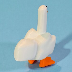 May include: A white goose figurine with orange feet and a black beak. The goose is standing on a light blue surface. The figurine is a 3D-printed object.