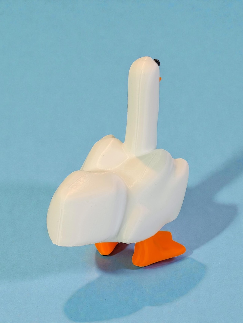 May include: A white goose figurine with orange feet and a black beak. The goose is standing on a light blue surface. The figurine is a 3D-printed object.