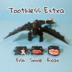 May include: A black dragon figure with outstretched wings, and three smaller dragon heads with different facial expressions. The text "Toothless Extra" is above the dragon, and "Fish Smile Roar" is below.