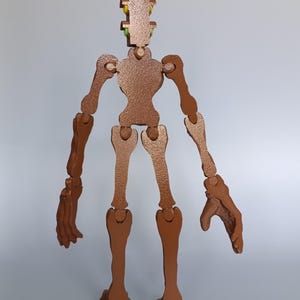 May include: A brown wooden articulated figure with a textured finish. The figure has a segmented design with movable joints, including arms, legs, and a head with colorful accents. The figure stands upright.
