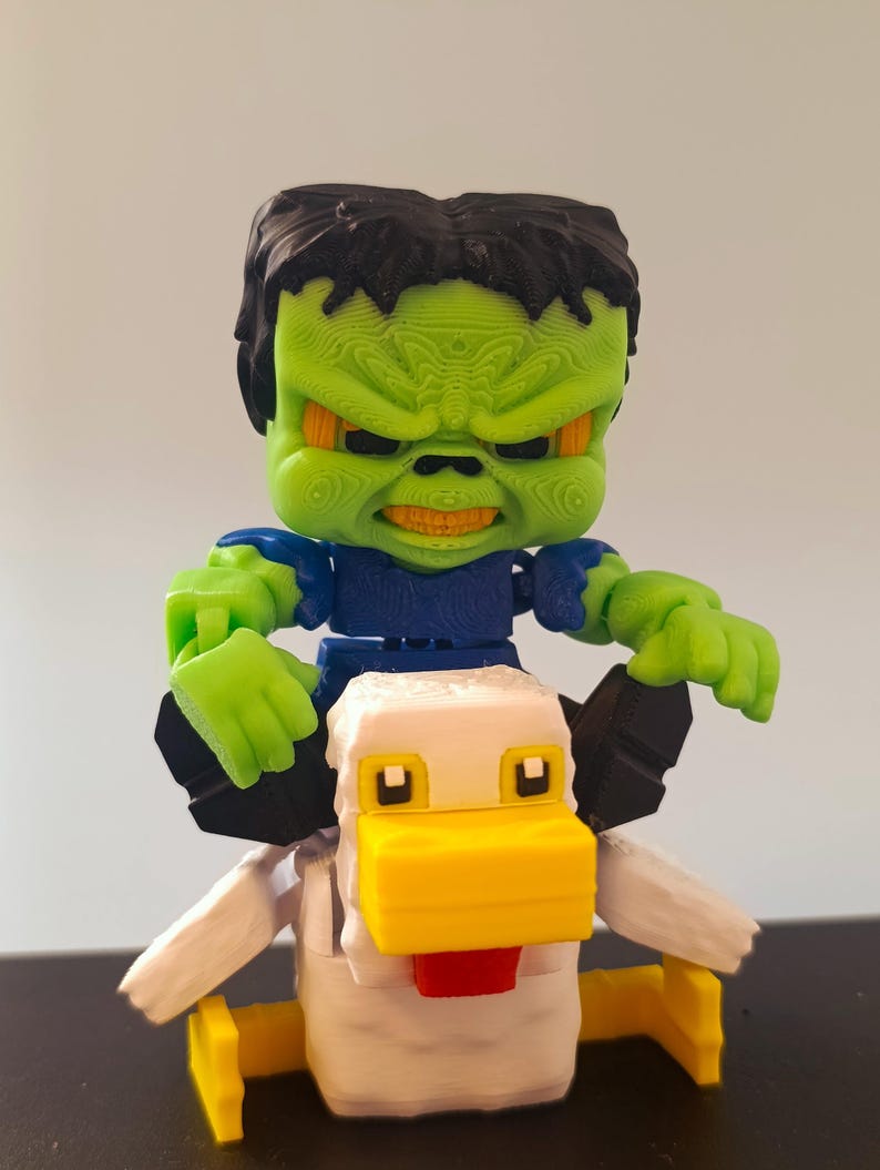 May include: A 3D-printed toy featuring a green-skinned figure with black hair and a stern expression, riding a white and yellow chicken. The figure is wearing a blue shirt and has green hands. The chicken has a yellow beak and red tongue.
