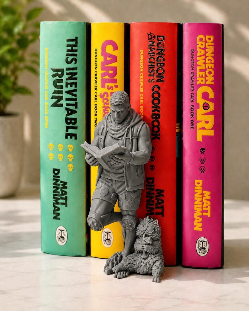 May include: A gray resin bookend featuring a standing figure reading a book, wearing a hooded vest and heart-patterned shorts, with a small furry creature wearing goggles at their feet, positioned in front of four Dungeon Crawler Carl books.