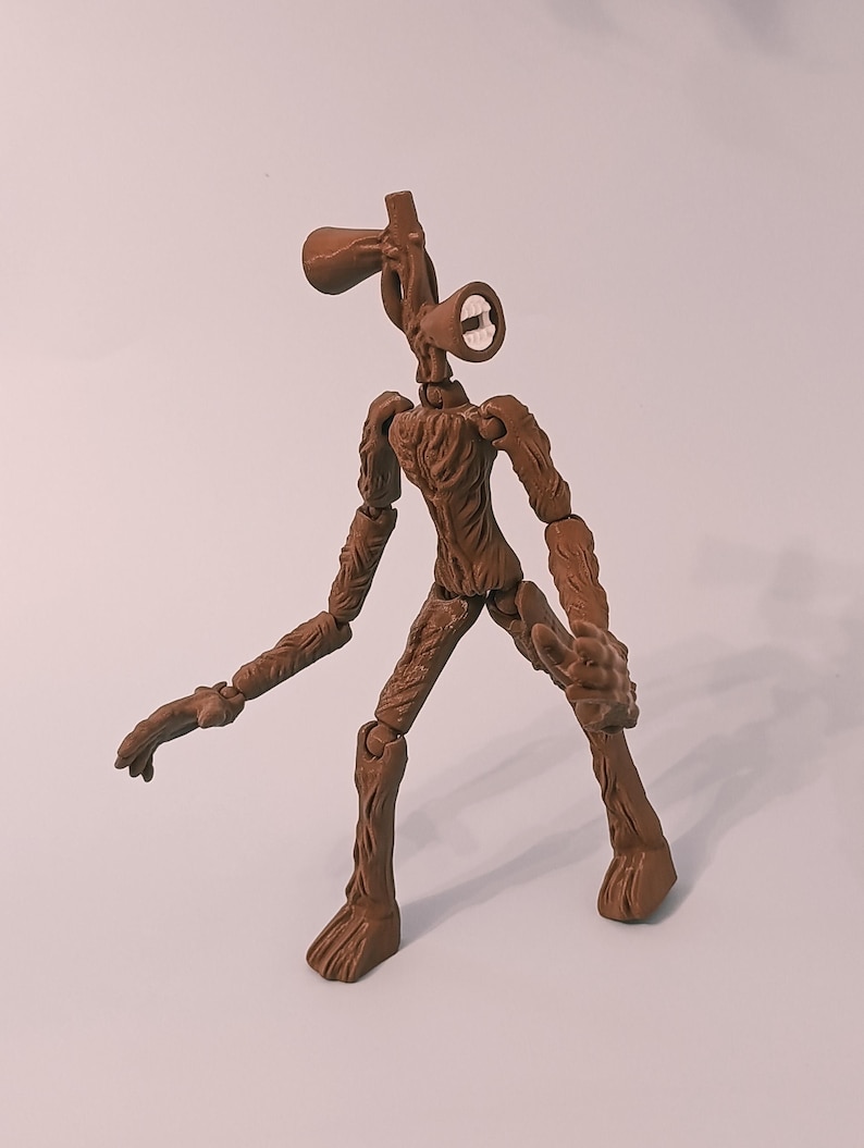 Op de afbeelding: Een bruin Siren Head actiefiguur met beweegbare gewrichten. De figuur heeft een gedetailleerd, gestructureerd ontwerp, met een hoofd in de vorm van twee sirenes. De figuur poseert met &eacute;&eacute;n arm uitgestrekt en de andere gebogen.