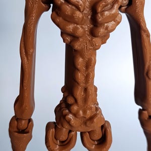 May include: A brown, articulated figure with a textured surface. The figure has a humanoid form with a detailed torso, arms, and legs. The joints are visible, suggesting a range of motion. The figure is made of a solid material.