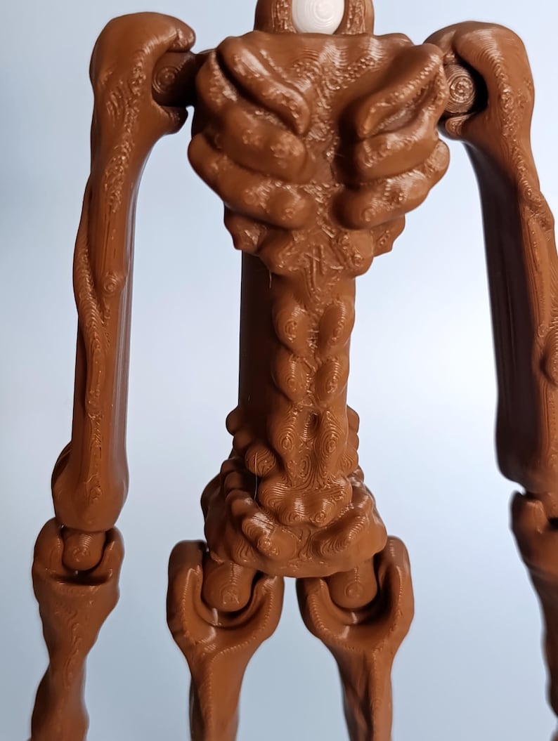 May include: A brown, articulated figure with a textured surface. The figure has a humanoid form with a detailed torso, arms, and legs. The joints are visible, suggesting a range of motion. The figure is made of a solid material.