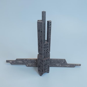 K&ouml;nnte beinhalten: Eine dunkelgraue, geometrische Skulptur mit einem vertikalen Turm und einer horizontalen Basis. Der Turm weist komplizierte Ausschnittmuster auf, und die Basis erstreckt sich auf beiden Seiten. Die Skulptur befindet sich vor einem hellblauen Hintergrund.