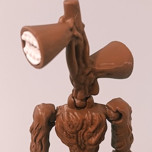 Op de afbeelding: Een bruin Siren Head actiefiguur met een gedetailleerd, gestructureerd ontwerp. De figuur heeft twee luidsprekerachtige hoofden met witte tanden, beweegbare armen en een menselijk torso. De figuur staat tegen een effen achtergrond.