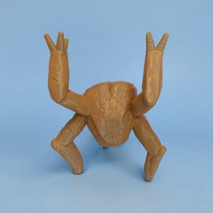 Pode incluir: Escultura impressa em 3D de cor castanha clara de uma criatura com quatro pernas e dois bra&ccedil;os levantados. A escultura tem uma superf&iacute;cie texturizada sobre um fundo azul claro.