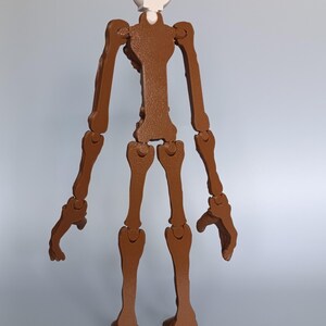 May include: A brown articulated skeleton figure with a white head. The figure is made of multiple pieces that are connected at the joints. The figure is standing upright against a light blue background.
