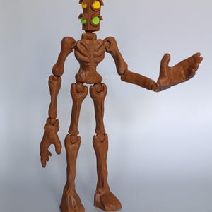 May include: A brown articulated figure with a traffic light head. The traffic light has red, yellow, and green lights. The figure has outstretched arms and a skeletal torso and limbs. The figure is standing on a white surface.