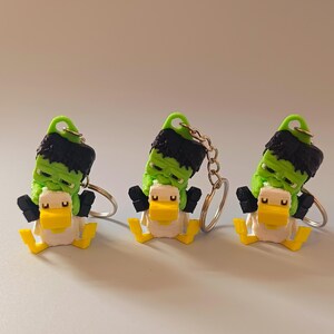 Op de afbeelding: Drie novelty sleutelhangers met een Frankenstein-monster eend ontwerp. De eenden hebben een witte body, gele snavel en poten en zwarte armen. De kop van het monster is groen met zwart haar en een groene lus voor de sleutelhangerring.