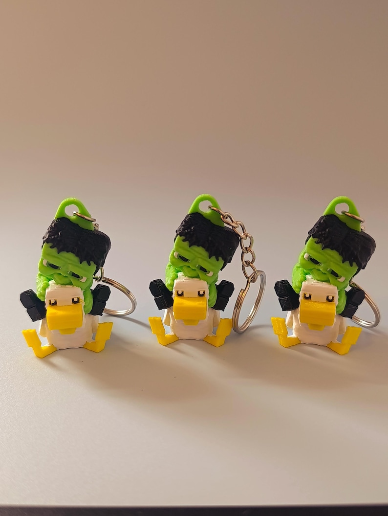 Op de afbeelding: Drie novelty sleutelhangers met een Frankenstein-monster eend ontwerp. De eenden hebben een witte body, gele snavel en poten en zwarte armen. De kop van het monster is groen met zwart haar en een groene lus voor de sleutelhangerring.
