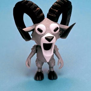 May include: A gray and white cartoon ram figurine with large black horns, big white eyes, and a wide open mouth. The ram has small arms and legs, and is standing on a blue surface.