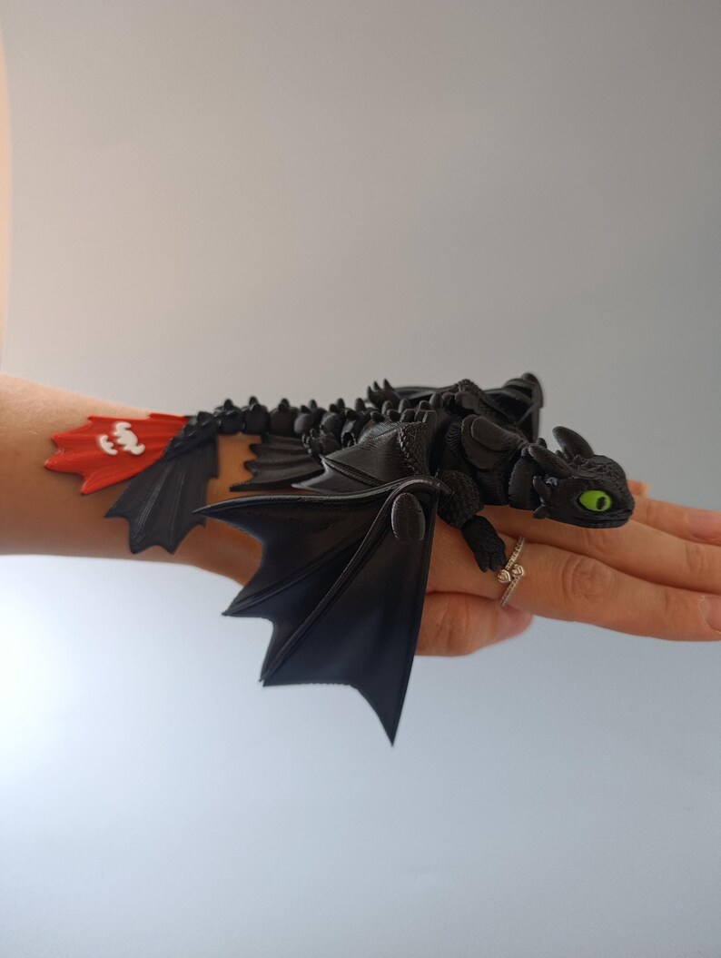 K&ouml;nnte beinhalten: Schwarze Drachenfigur mit gr&uuml;nen Augen und roter und wei&szlig;er Schwanzflosse. Der Drache hat detaillierte Fl&uuml;gel und ist auf einer Hand platziert. Das Objekt hat ein Fantasy-Thema.
