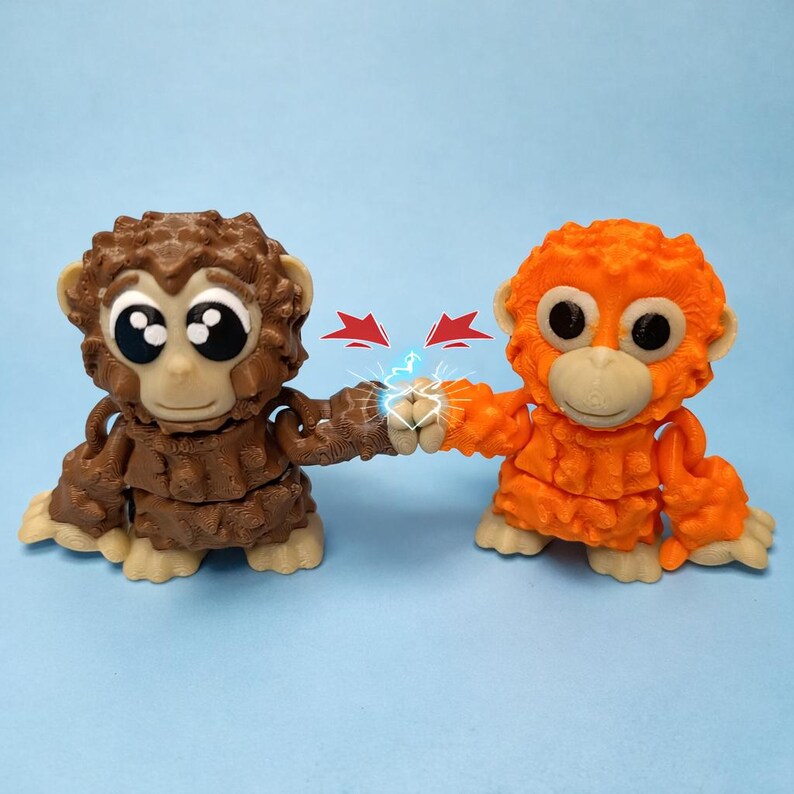 May include: Two toy orangutans, one brown and one orange, are fist-bumping. The brown orangutan is on the left, and the orange one is on the right. Both have large, expressive eyes and are in a playful pose. Red arrows and blue lightning bolts are between their fists.