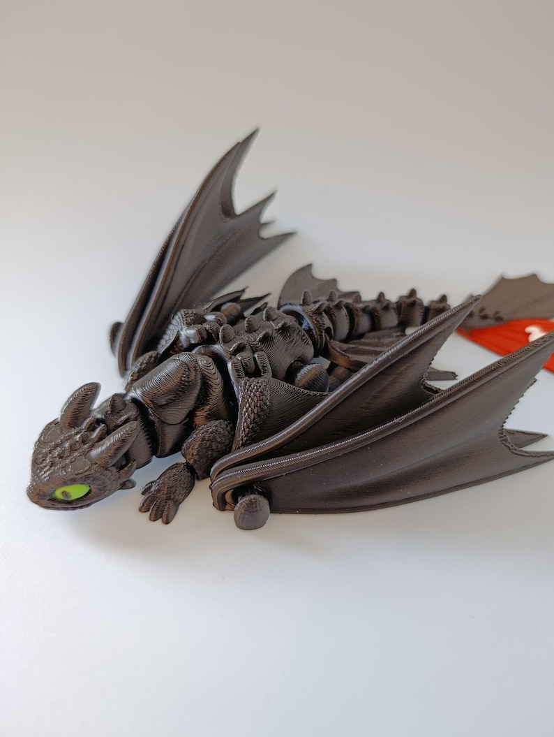 K&ouml;nnte beinhalten: Dunkelbraune Drachenfigur mit beweglichen Fl&uuml;geln und Gliedma&szlig;en. Der Drache hat gr&uuml;ne Augen und einen detaillierten, strukturierten K&ouml;rper. Die Fl&uuml;gel sind ausgebreitet, und der Drache liegt. Die Figur ist wahrscheinlich ein Sammlerst&uuml;ck oder ein Spielzeug.