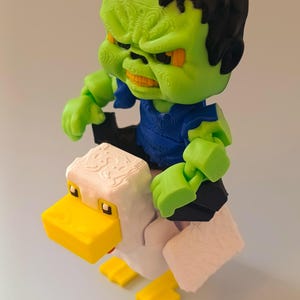 May include: A 3D-printed figurine of a green-skinned monster with black hair and a blue shirt riding a white and yellow duck. The monster has an angry expression. The duck has a yellow beak and feet.