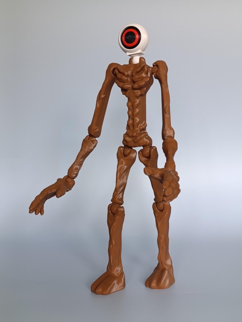 May include: A brown articulated figure with a large eye for a head. The eye is white with a red and black iris. The figure has a skeletal appearance with jointed limbs and feet. The figure is standing against a light gray background.