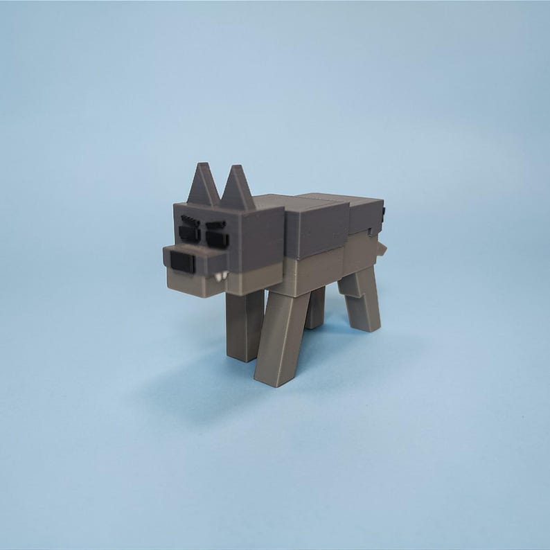Op de afbeelding: Een grijze en bruine blokstijl wolf figuur tegen een lichtblauwe achtergrond. De speelgoedwolf heeft een donkergrijze kop en rug, met een lichtere bruine lichaam en poten.