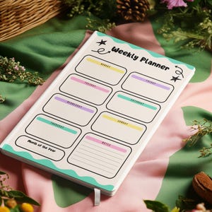 Puede incluir: Un cuaderno de planificación semanal con cubierta color crema que presenta el texto Weekly Planner, iconos de estrellas negras y un borde ondulado turquesa. El diseño interior incluye recuadros para cada día con detalles en amarillo, rosa y morado.