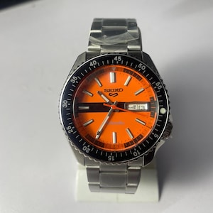 Reloj automático Seiko 5 Sports – Esfera naranja, acero inoxidable, día/fecha, estilo buceo