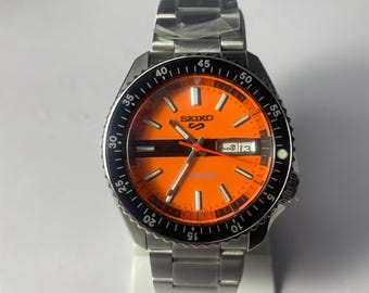 Reloj automático deportivo Seiko 5: esfera naranja, acero inoxidable, día/fecha, estilo buceador.