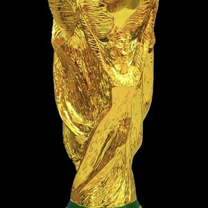 May include: A gold-coloured trophy featuring two human figures with arms raised, supporting a globe at the top. The base is circular with two horizontal green bands and the embossed text "FIFA WORLD CUP" visible on the front surface.