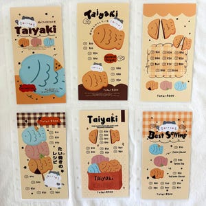 May include: A collection of six illustrated cards featuring Taiyaki, a Japanese fish-shaped cake. Each card has a unique design with fish illustrations, prices, and text. The color palette includes beige, orange, and blue, with cat illustrations.