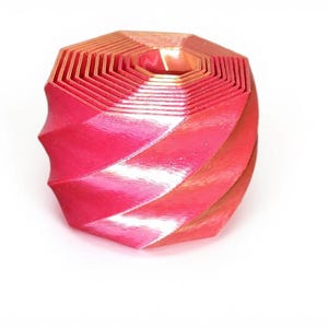 May include: A red and orange geometric sculpture with a spiral design. The object has a layered construction with a hexagonal top and a twisted, ridged body. The color gradient shifts from red to orange.